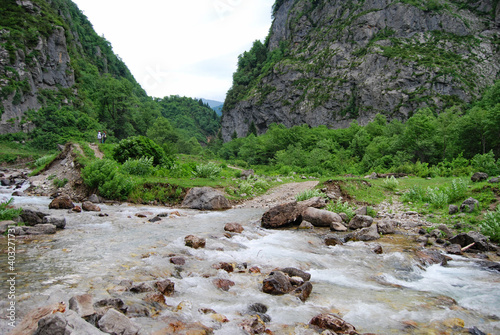 The Gega mountain River flows between the mountains. Fast mountain river. The rocky shore. On the left are small figures of tourists. photo