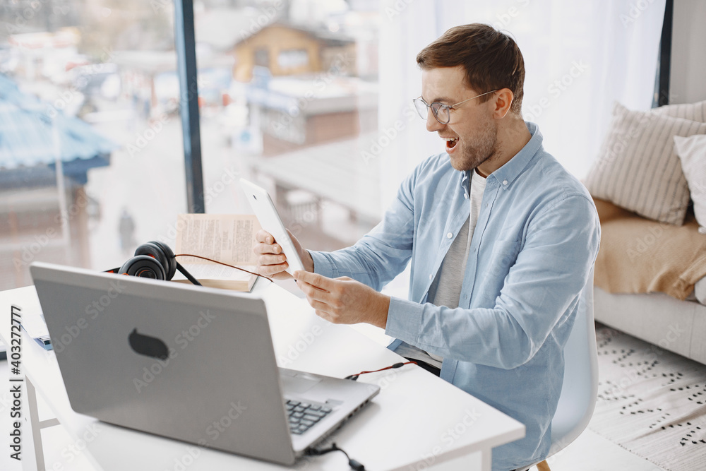 Man sitting in living room at home. Guy enjoying studying using laptop and headset. Man use a tablet. Man sitting in living room at home. Guy enjoying studying using laptop and headset. Man use a tablet.