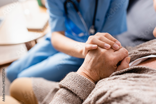 partial view of nurse touching hands of aged patient in nursing home  blurred background