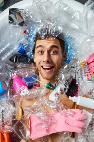 happy male lie aroung plastic waste, enjoy, smiel at camera, in room full of trash. ecological problem concept photo