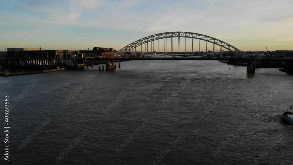 fully loaded barge with mudd navigating on a dutch river between the pillars of a brigde during golden hour. Drone truck shot fully loaded barge with mudd navigating on a dutch river between the pillars of a brigde during golden hour. Drone truck shot
