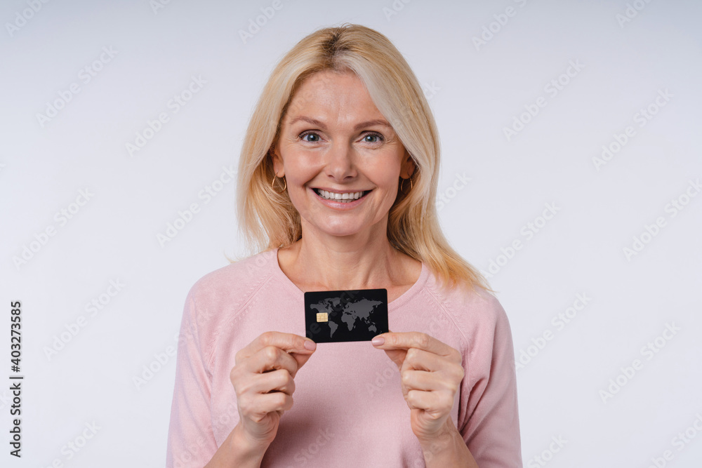Happy middle-aged european woman showing credit card isolated over grey background Happy middle-aged european woman showing credit card isolated over grey background