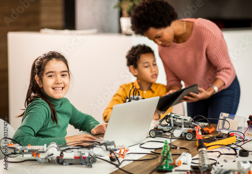 Happy kids with their African American female science teacher with laptop programming electric toys and robots at robotics classroom