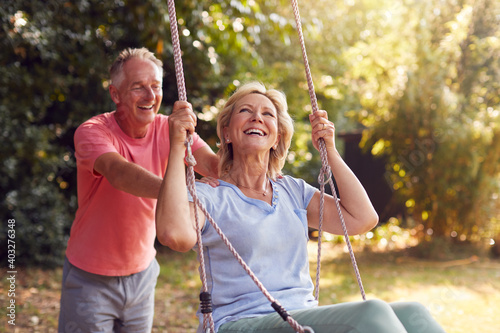 Retired Couple Having Fun With Man Pushing Woman On Garden Swing