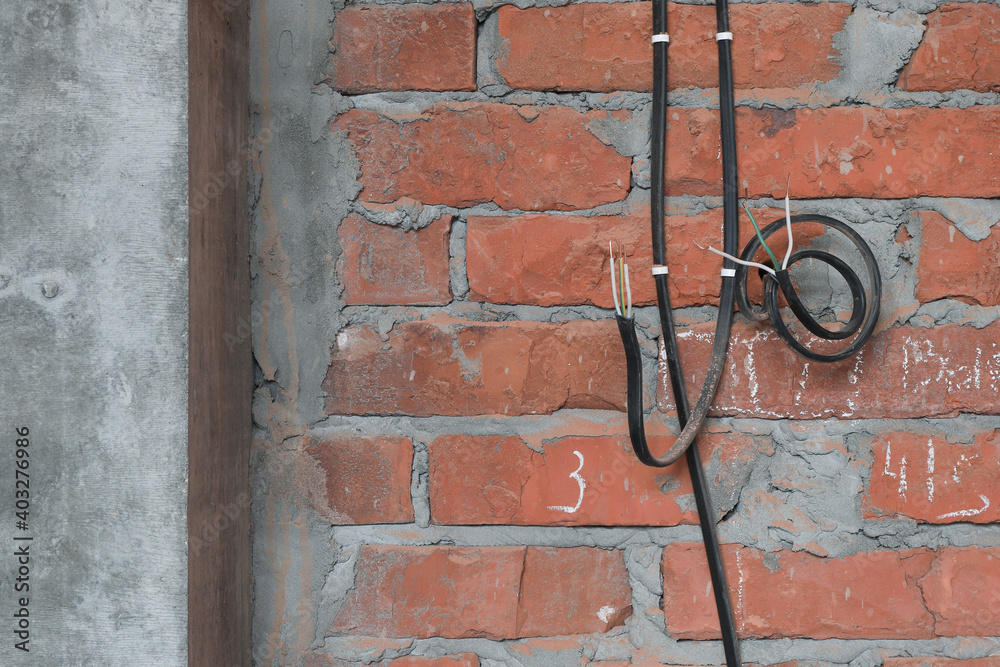 electrical cables are fixed to a brick wall for future outlets next to a concrete column