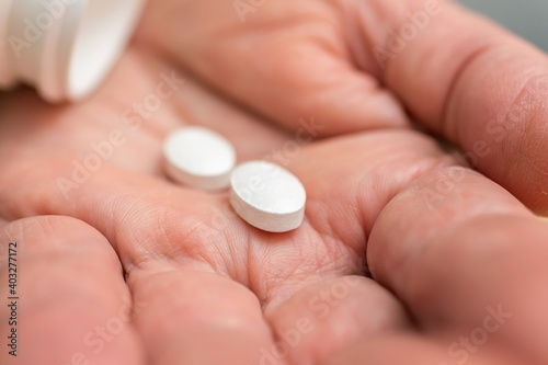 White pills of painkiller or antibiotic for treatment on senior woman hand palm, medicines and vitamin supplements concept, close-up view
