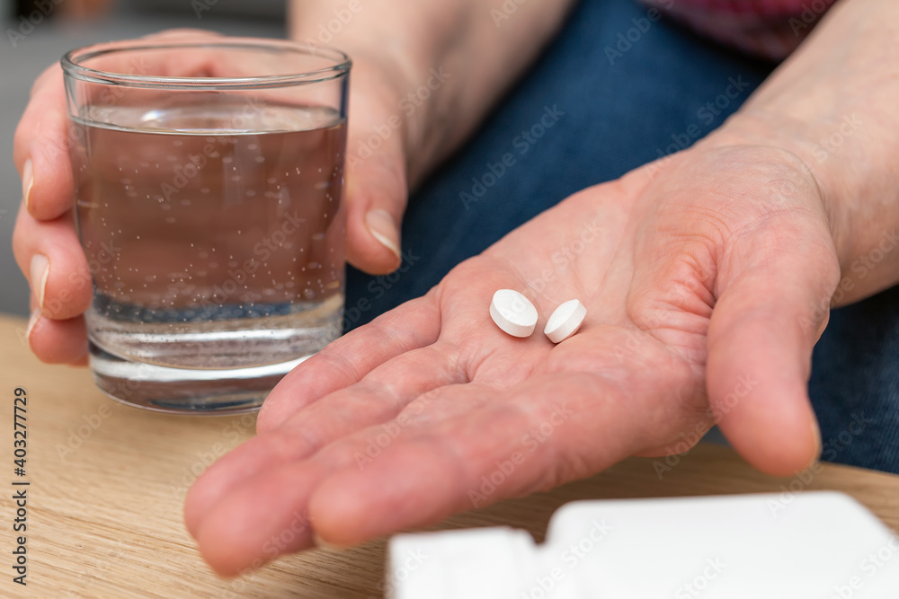 White pills of painkiller or antibiotic for treatment on senior woman hand palm, glass with water, medicines and vitamin supplements concept,close-up view White pills of painkiller or antibiotic for treatment on senior woman hand palm, glass with water, medicines and vitamin supplements concept,close-up view