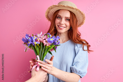 woman is happy to get flowers by suitors, smile, wearing summer dress and hat, isolated pink background