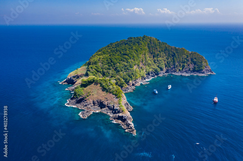 Aerial drone view of boats around a beautiful, remote tropical island in a blue ocean