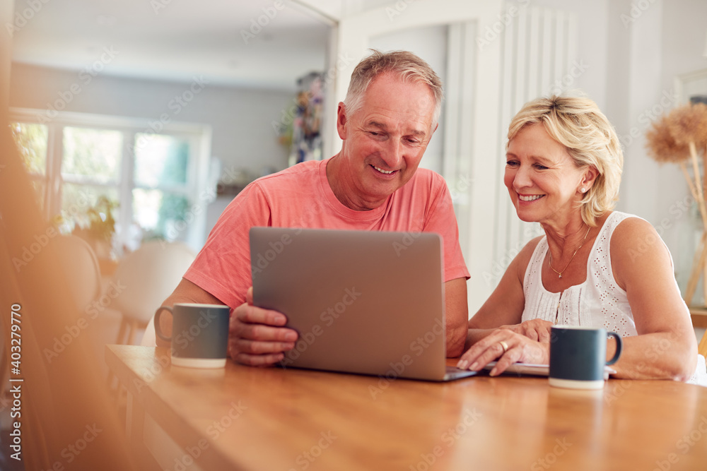 Retired Couple At Home In Kitchen Using Laptop To Shop Online Or Make Video Call Retired Couple At Home In Kitchen Using Laptop To Shop Online Or Make Video Call