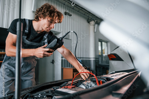 Tests car's electronics. Adult man in grey colored uniform works in the automobile salon