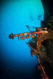 A large, upturned shipwreck on the sea floor near a tropical coral reef
