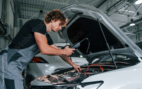 Tests car's electronics. Adult man in grey colored uniform works in the automobile salon