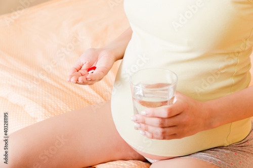 Beautiful woman sitting on sofa holding a pill and water © sosiukin