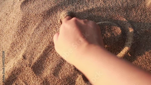 Close up view of woman hand drawing heart with finger on the sand at the beach. love vaentine's day concetp. photo