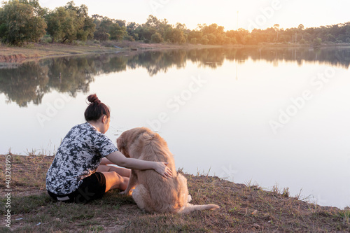 Woman and Golden retriever dog sitting near river or lake