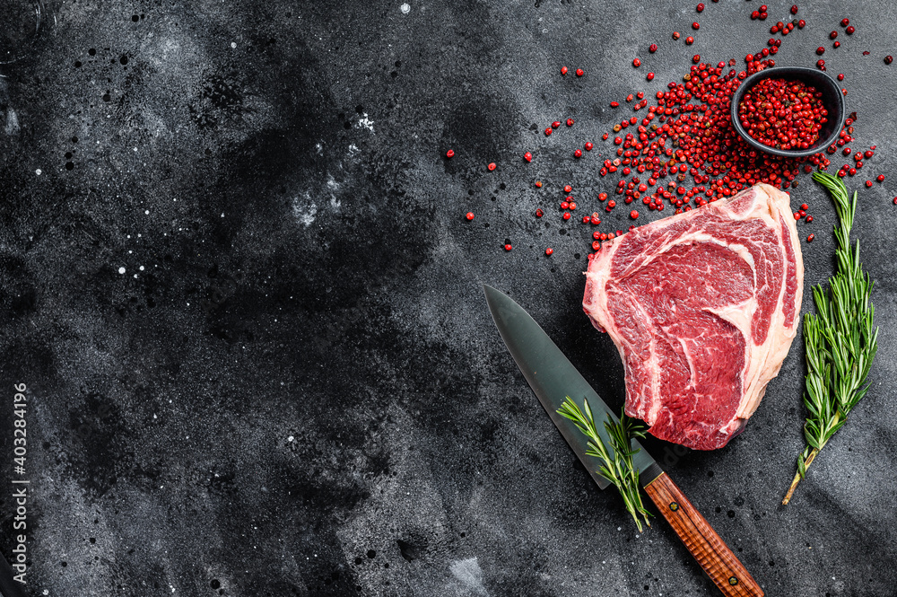 Raw cowboy steak or ribeye on the bone with herbs. Marble beef. Black background. Top view. Copy space.