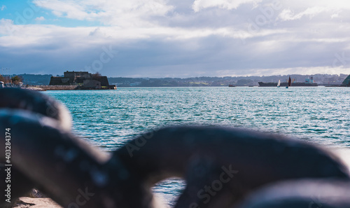 Beautiful maritime landscape of the city of Coruña. In a blurred foreground you can see a chain, and in a focused background you can see a cloudy sky, the castle of San Anton, the sea and some ships