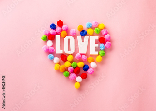 Bright creative card for Valentine's Day. The inscription Love in the heart made of multi-colored pom-poms on a pink background. Valentines day creative concept