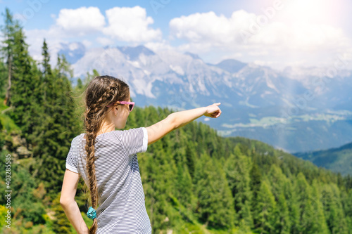 Girl hiking on beautiful summer day in alps mountains Austria, resting on rock and admire amazing view to mountain peaks. Active family vacation leisure with kids. Outdoor fun and healthy activity