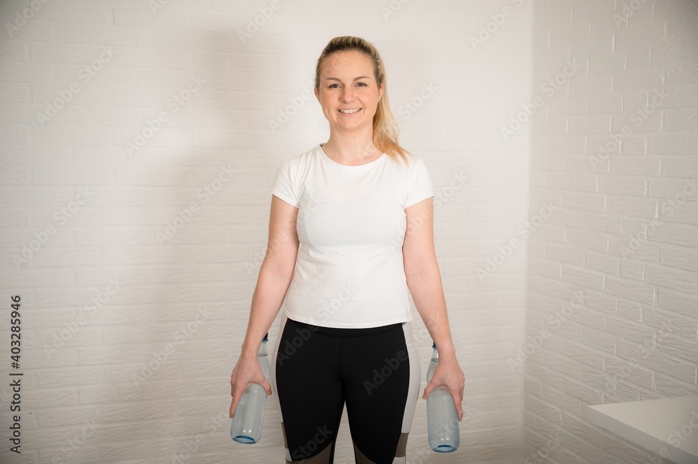 Happy blonde woman doing fitness exercise with water bottles - basic sport workout as a training at home