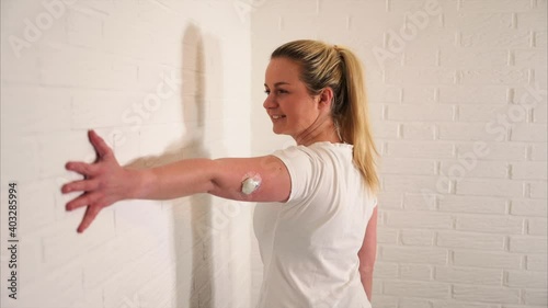 Happy blonde woman with diabetes sensor doing basic fitness exercise and warm-up as a training at home photo