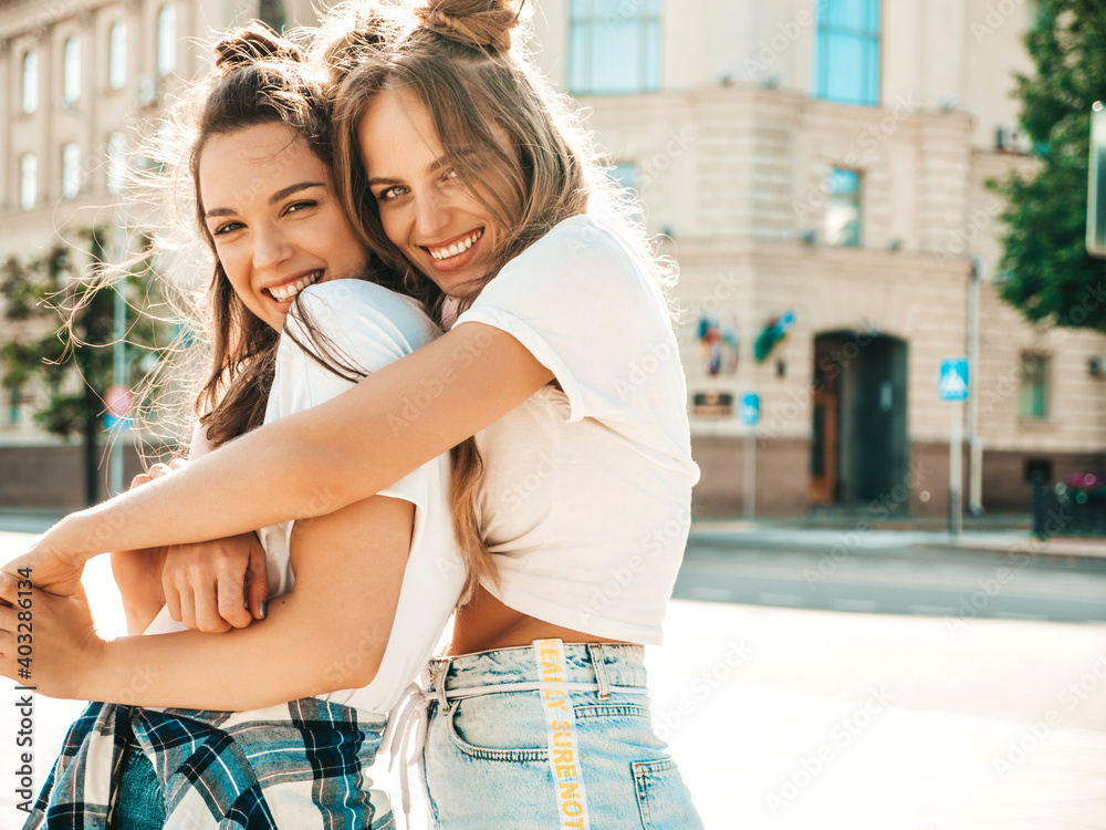 Portrait of two young beautiful smiling hipster female in trendy summer white t-shirt clothes.Sexy carefree women posing on street background. Positive models having fun and hugging
