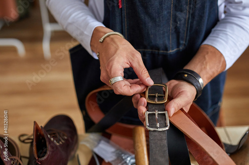 close-up photo of crafstman comparing leather belts during work in workshop, professional making leather things for customers