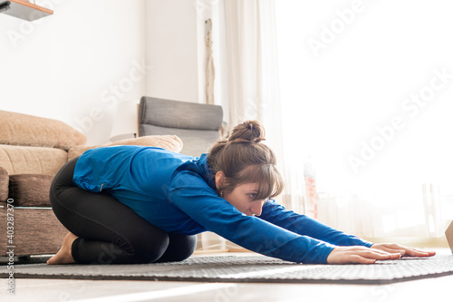 Young woman in sportswear practicing yoga and stretching exercises in living room, woman on sports mat in brightly lit room, relaxation concept