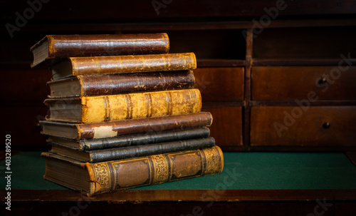 Vintage books stack on old wooden surface in warm directional light. Selective focus.