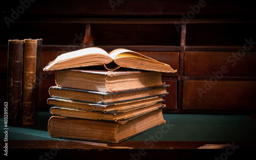A stack of old books. Vintage book on wooden table. Magic lightning around a glowing book in the room of darkness. Selective focus