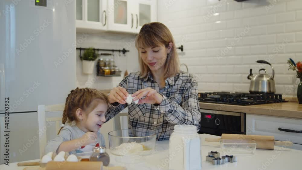 Young family spending time at home together. Mother and daughter having fun baking cooking christmas cookies pastry in the kitchen. Loving happy mom teaches cute kid to knead dough. Young family spending time at home together. Mother and daughter having fun baking cooking christmas cookies pastry in the kitchen. Loving happy mom teaches cute kid to knead dough.