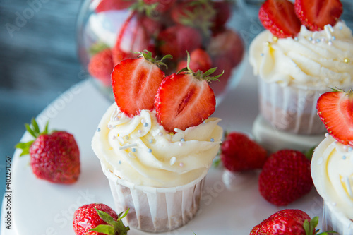 cupcake in the center with white cream decorated with ripe strawberries on a gray blue background and scattered strawberries.