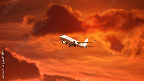 Zoom photo of modern passenger airplane flying towards sunset with cloudy sky and beautiful golden colors