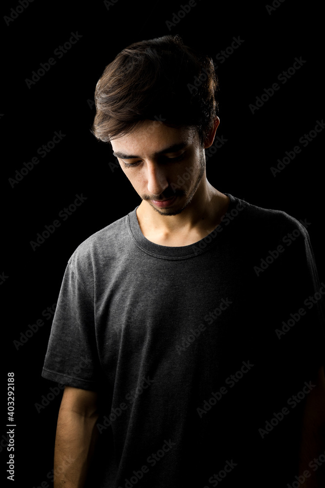 Young man portrait with a grey shirt looking down. low key photography. black background Young man portrait with a grey shirt looking down. low key photography. black background