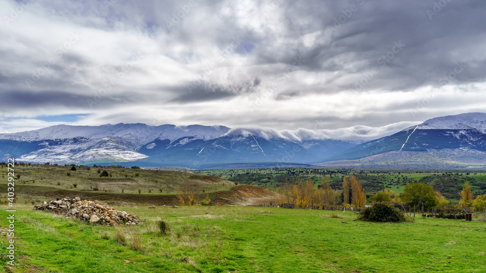 Green landscape with snowy mountains and dramatic sky in Somosierra Madrid.
