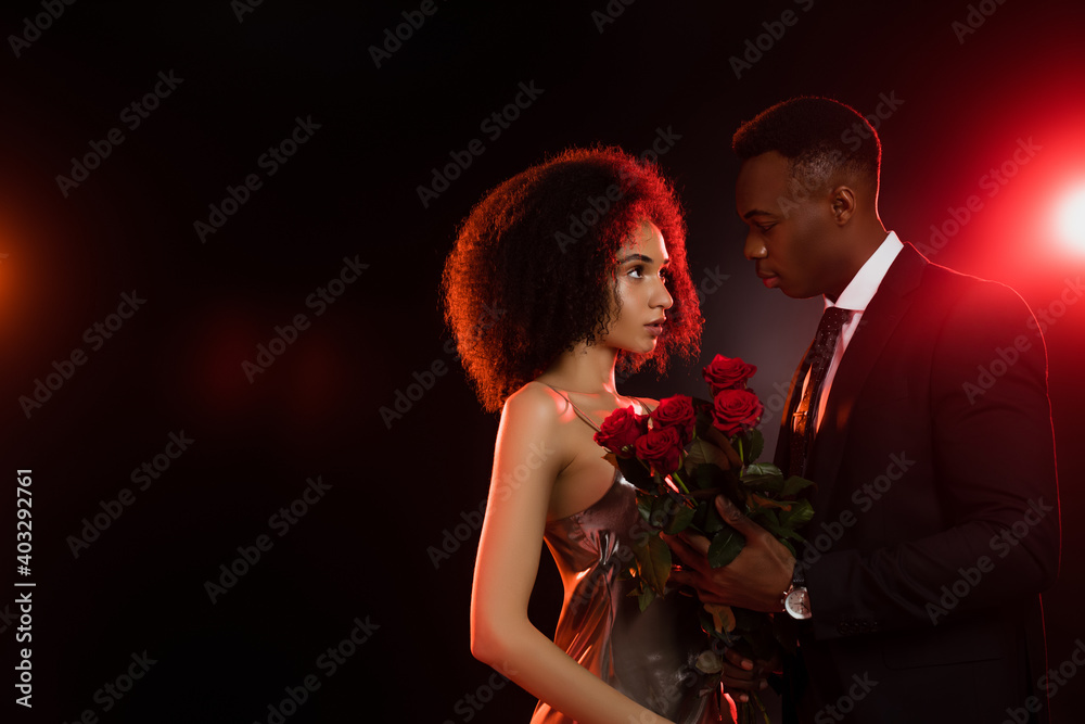 curly african american woman with red roses looking at boyfriend in suit on black curly african american woman with red roses looking at boyfriend in suit on black