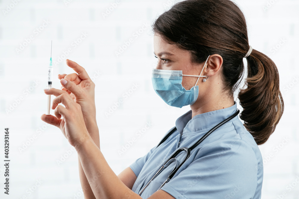 Beautiful female doctor with medical mask. Portrait of nurse with syringe in her hand.