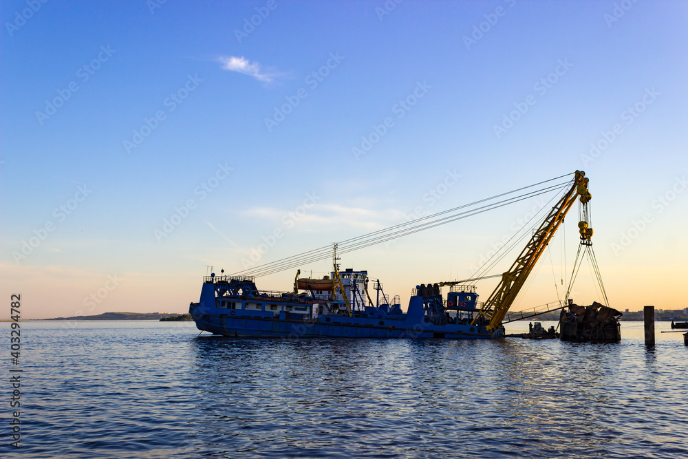 A river crane retrieves an object from the bottom of the river near the embankment.