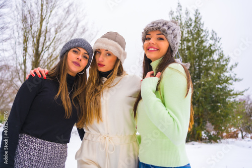 Winter lifestyle, young caucasian friends with winter outfit and wool hats enjoying the snow next to snowy pine trees, holidays in nature