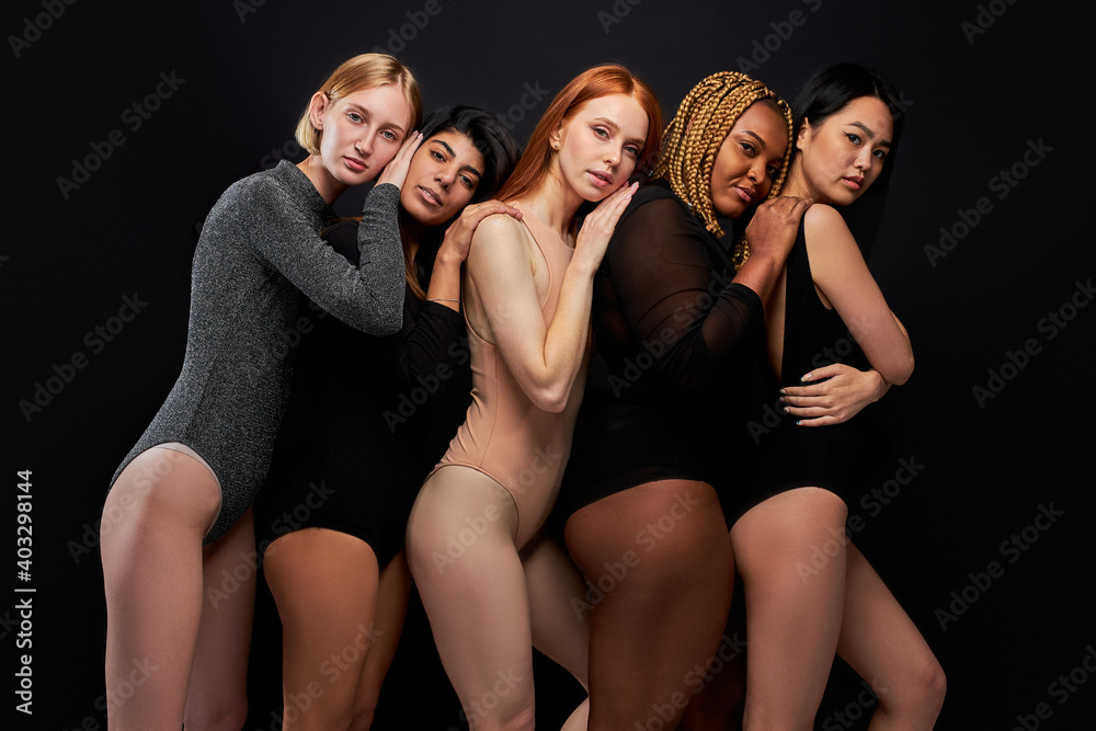 group of models posing at camera, diverse females leaned on each other, wearing bodysuit, isolated on black background group of models posing at camera, diverse females leaned on each other, wearing bodysuit, isolated on black background