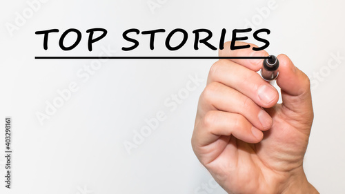 the hand writes text TOP STORIES with a marker on a white background. business concept