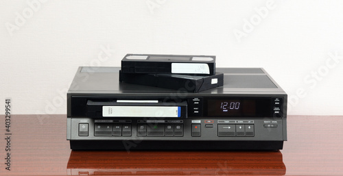An old vintage videotape recorder from the 1980s stands on a dark table with a videotape. Retro VCR. photo