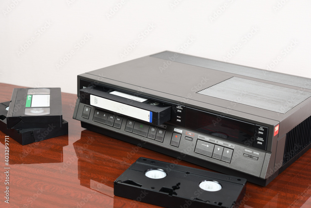 Obraz premium An old vintage videotape recorder from the 1980s stands on a dark table with a videotape. Retro VCR.