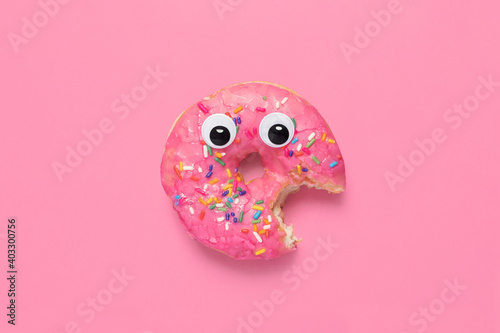 Shocked partially eaten pink donut doughnut on a matching pink background with googly eyes and copy space and room for text.