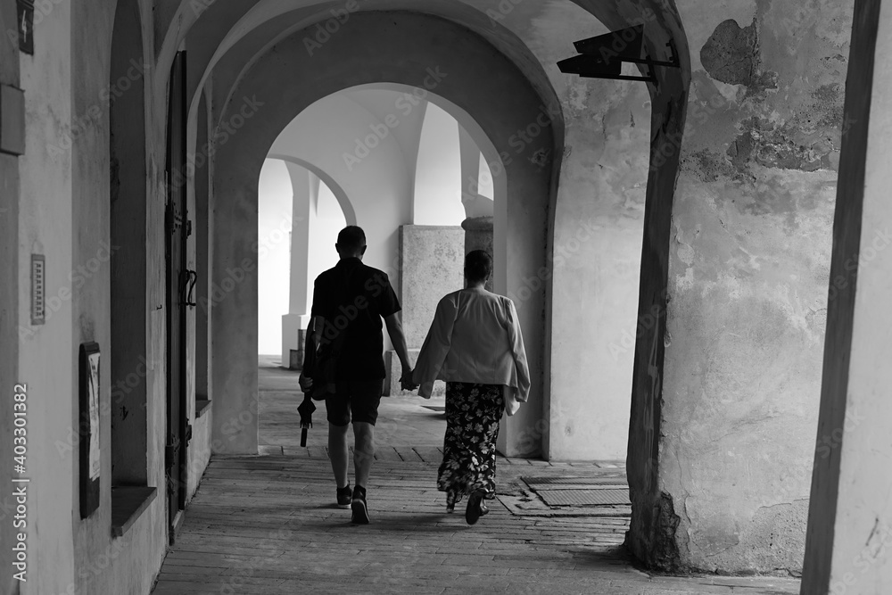 Middle aged couple holding hands walking in historic city arcade, black and white photo