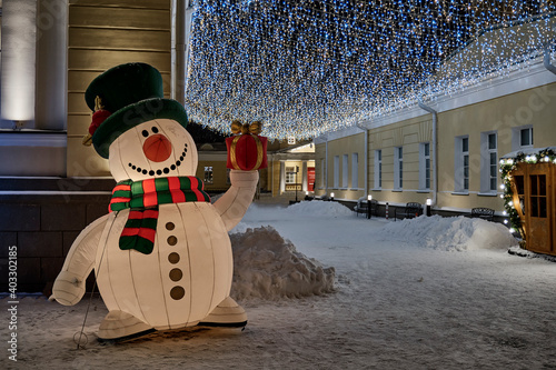 Big colorful funny inflatable decorative snowman on a winter evening illuminated city street. photo