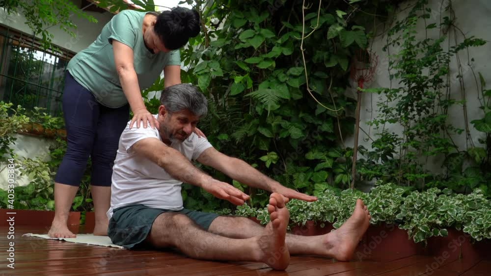 Pareja de mediana edad con ropa deportiva ayudándose para estirar en el jardín de sus casa