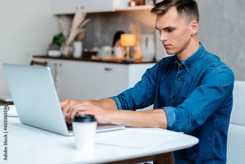 young man is working on a laptop in his kitchen. young man is working on a laptop in his kitchen.
