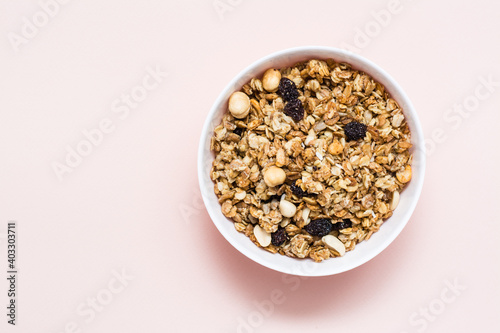 Healthy eating. Baked oats, nuts and raisins granola in a bowl on a pink background. Top view